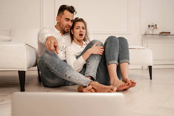 Man pointing with finger near shocked girlfriend while watching movie on blurred laptop — Stock Photo