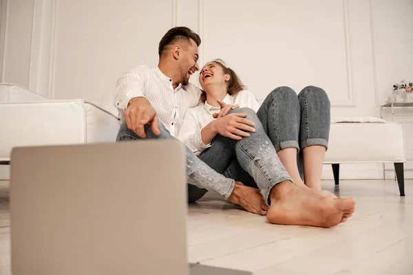 Glückliches Paar schaut Komödie auf Laptop, während es auf dem Boden sitzt, verschwommener Vordergrund — Stockfoto