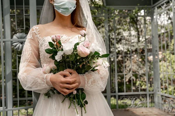 Cropped view of elegant bride in medical mask holding wedding bouquet in park — Stock Photo