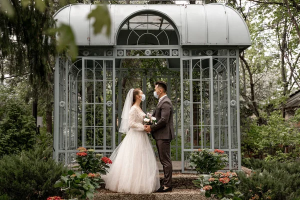 Full length view of newlyweds in medical masks looking at each other outdoors — Photo de stock