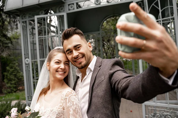 Happy man taking photo with cheerful bride on digital camera, blurred foreground — Fotografia de Stock