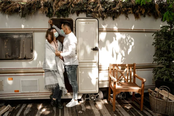 Young couple in medical masks talking near trailer in camping — Stock Photo