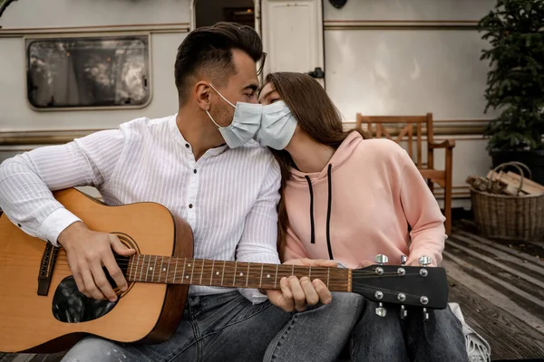 Young man in medical mask kissing girlfriend and playing guitar in camping — Foto stock