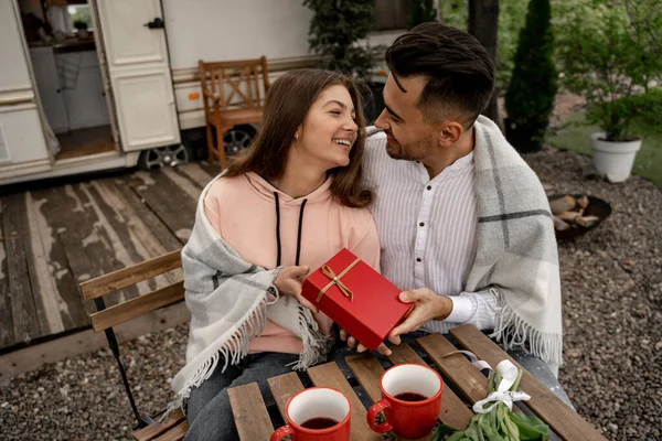 Man presenting gift to happy woman near coffee on table in camping - foto de stock