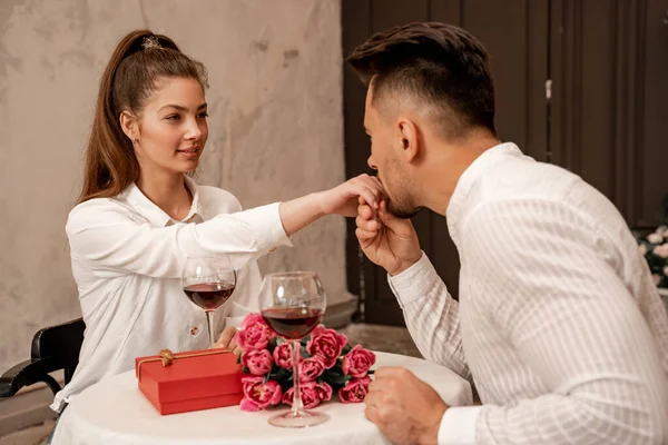 Man kissing hand of pretty woman near wine glasses, present and bouquet in restaurant — Photo de stock