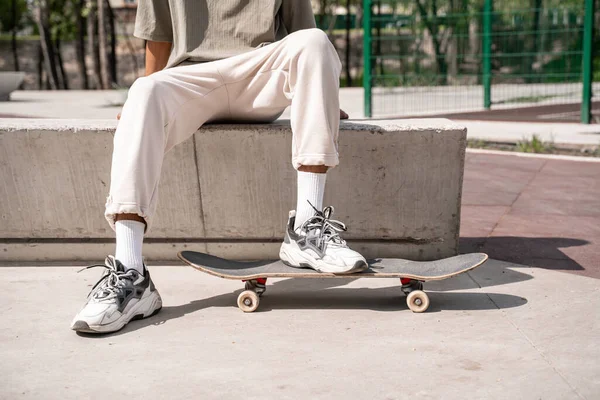 Vista ritagliata di uomo africano americano seduto sul confine vicino skateboard all'aperto — Foto stock
