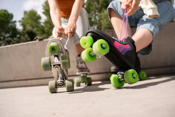 Cropped view of blurred women tying laces on roller skates in park — Stock Photo