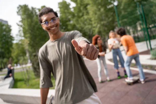Blurred african american man showing thumb up near blurred skaters in park — Stock Photo