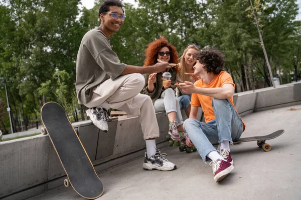 Uomo afroamericano sorridente seduto sul confine vicino skate e amici felici — Foto stock