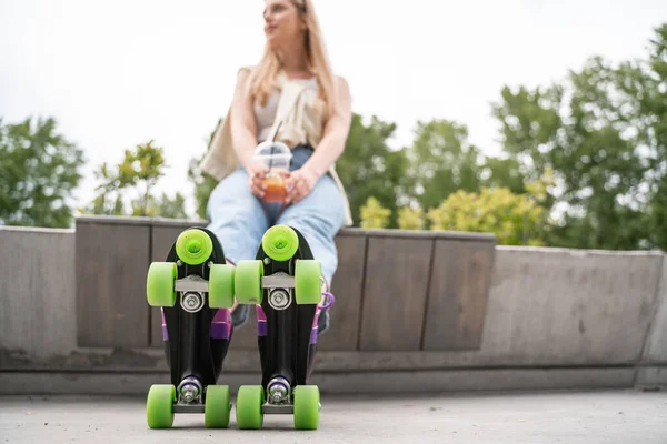 Mulher desfocada em patins sentados no banco de fronteira ao ar livre — Fotografia de Stock