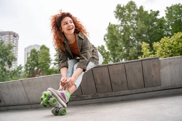 Excited woman looking away while tying laces on roller skate on border bench in park — Stock Photo