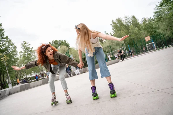 Happy friends holding hands while rollerblading in skate park — Stock Photo