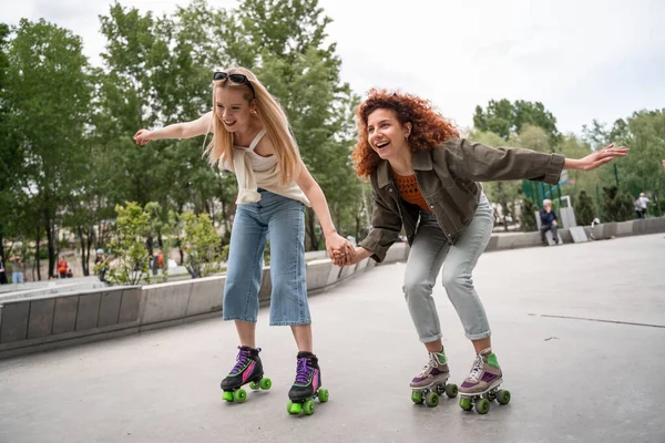 Excited women holding hands while rollerblading in park — Stock Photo