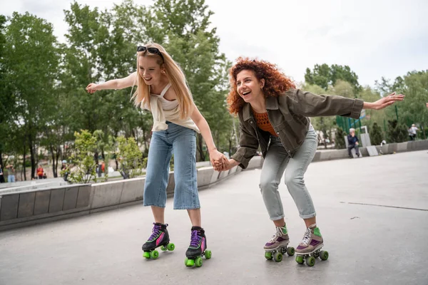 Excitées femmes tenant la main tandis que le roller dans le parc — Photo de stock