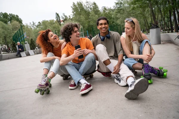 Lockiger Mann mit tragbarem Musiklautsprecher, der in der Nähe multiethnischer Freunde auf Asphalt sitzt — Stockfoto