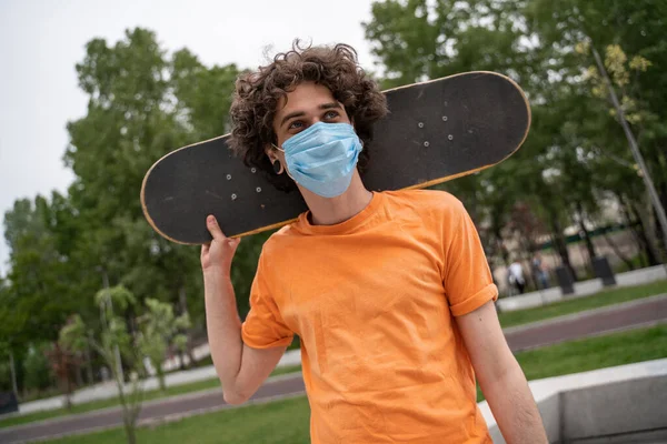 Jovem homem em máscara de segurança olhando para longe enquanto segurando skate atrás do pescoço — Fotografia de Stock