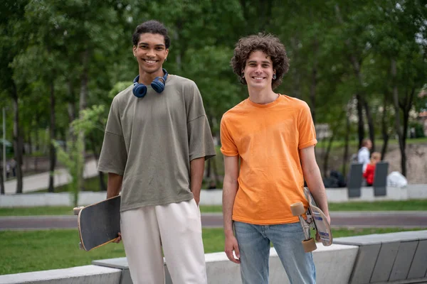 Alegre interracial amigos com skates sorrindo para câmera ao ar livre — Fotografia de Stock