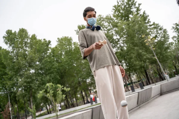Jovem homem americano africano em máscara protetora jogando jogo de kendama no parque — Fotografia de Stock