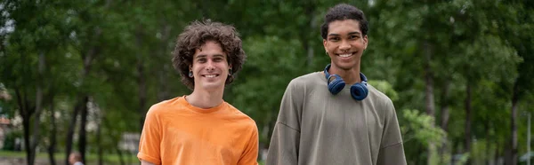 Jovem e feliz interracial homens olhando para câmera ao ar livre, banner — Fotografia de Stock