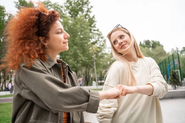 Fröhliche junge Frauen, die einander anlächeln und draußen Faustpumpen machen — Stockfoto