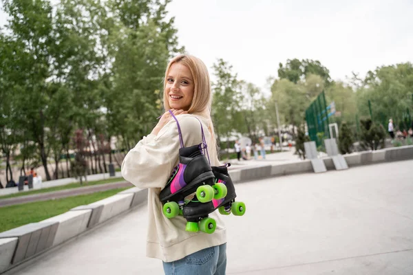 Young blonde woman with rollers skates looking at camera in skate park — Stock Photo