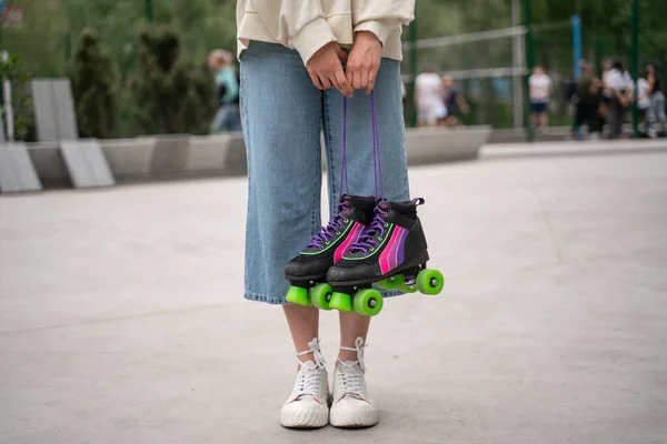 Partial view of woman in jeans and sneakers holding roller skates — Stock Photo