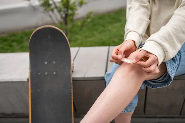 Vista recortada del skateboarder aplicando yeso adhesivo sobre la rodilla lesionada - foto de stock