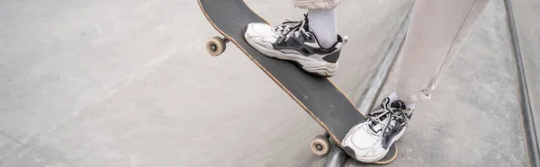 Partial view of man in sport shoes riding skateboard on skate ramp, banner — Stock Photo