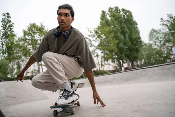 Jeune homme afro-américain équitation skateboard dans squat pose — Photo de stock