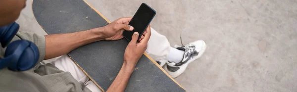 Vista parcial del patinador afroamericano usando smartphone con pantalla en blanco al aire libre, banner - foto de stock