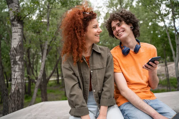 Hombre sonriente con teléfono inteligente hablando con la mujer rizada en el parque - foto de stock