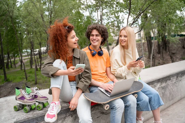 Happy friends with gadgets talking while spending time in skate park — Stock Photo