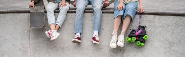 Partial view of interracial skaters in sneakers sitting on skate ramp, banner — Stock Photo