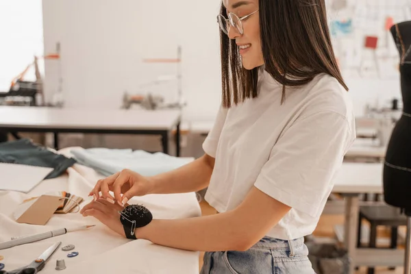 Side view of smiling asian designer with pincushion in studio — Stock Photo