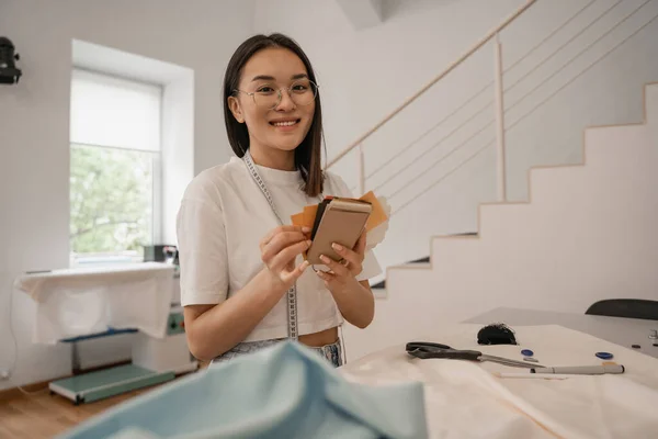 Designer asiatico sorridente a fotocamera mentre tenendo colore campioni — Foto stock