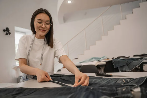 Junge asiatische Designerin misst Tuch auf Tisch — Stockfoto