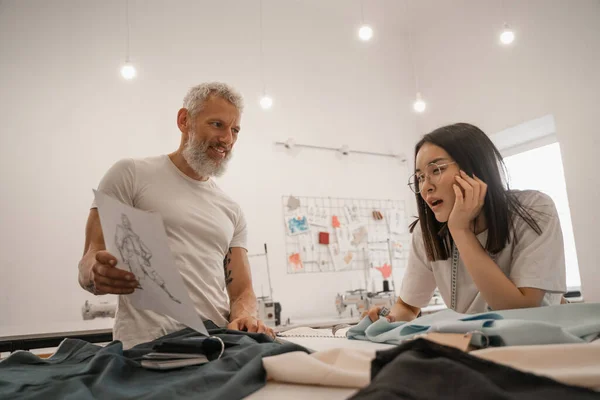 Smiling designer holding sketch near asian colleague — Stock Photo