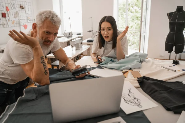 Verblüffter asiatischer Designer blickt auf Laptop neben Kollegin — Stockfoto