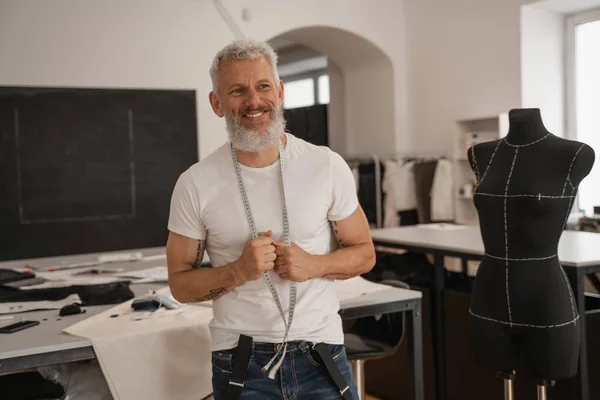 Lächelnder reifer Designer hält Maßband neben Schaufensterpuppe — Stockfoto