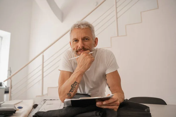 Smiling designer with pencil and clipboard looking at camera in studio — Stock Photo