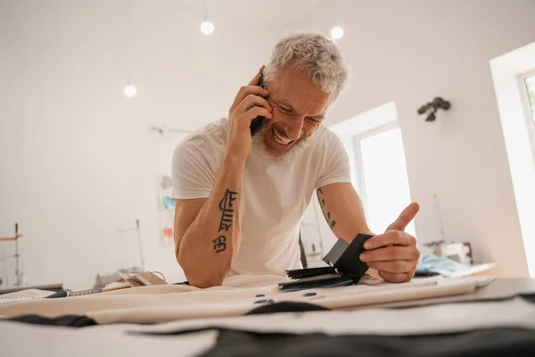 Smiling designer talking on smartphone near color swatches and cloth — Stock Photo