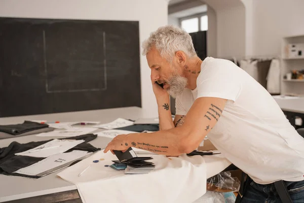 Side view of mature designer talking on mobile phone near color swatches — Stock Photo