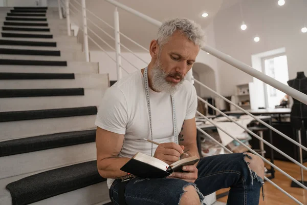 Diseñador maduro escribiendo en el cuaderno en las escaleras - foto de stock