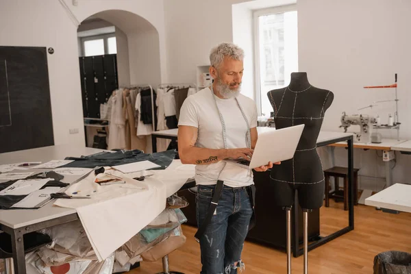 Designer usando laptop perto de manequim em estúdio — Fotografia de Stock