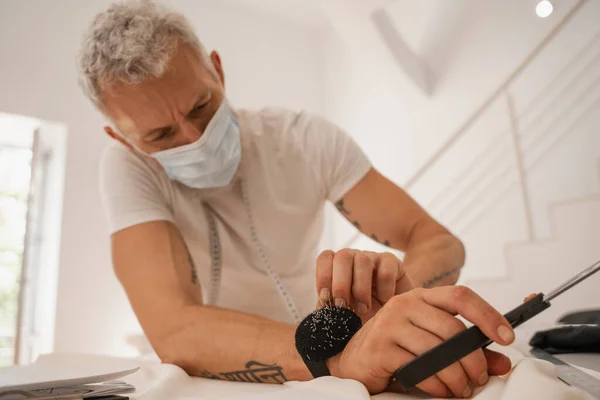 Nadelkissen am Arm des Designers in medizinischer Maske bei der Arbeit im Studio — Stockfoto