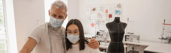 Diseñadores multiétnicos con máscaras protectoras de pie en el taller, pancarta - foto de stock