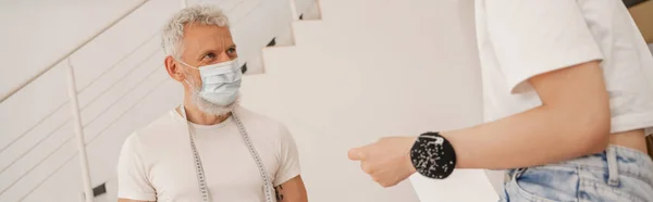 Designer in medical mask looking at colleague with pincushion, banner — Stock Photo