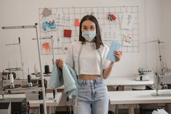 Asian designer in medical mask holding cloth in atelier — Stock Photo