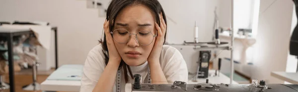 Exhausted asian seamstress sitting near sewing machine in atelier, banner — Stock Photo