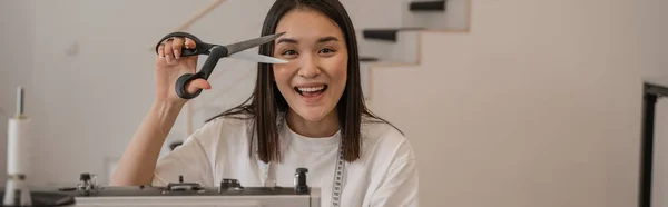 Smiling asian designer holding sewing scissors in studio, banner — Stock Photo